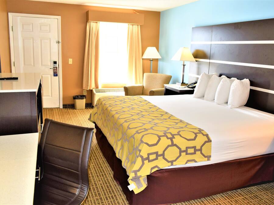A hotel room with a bed, a desk, a chair, a TV, and a window with curtains.