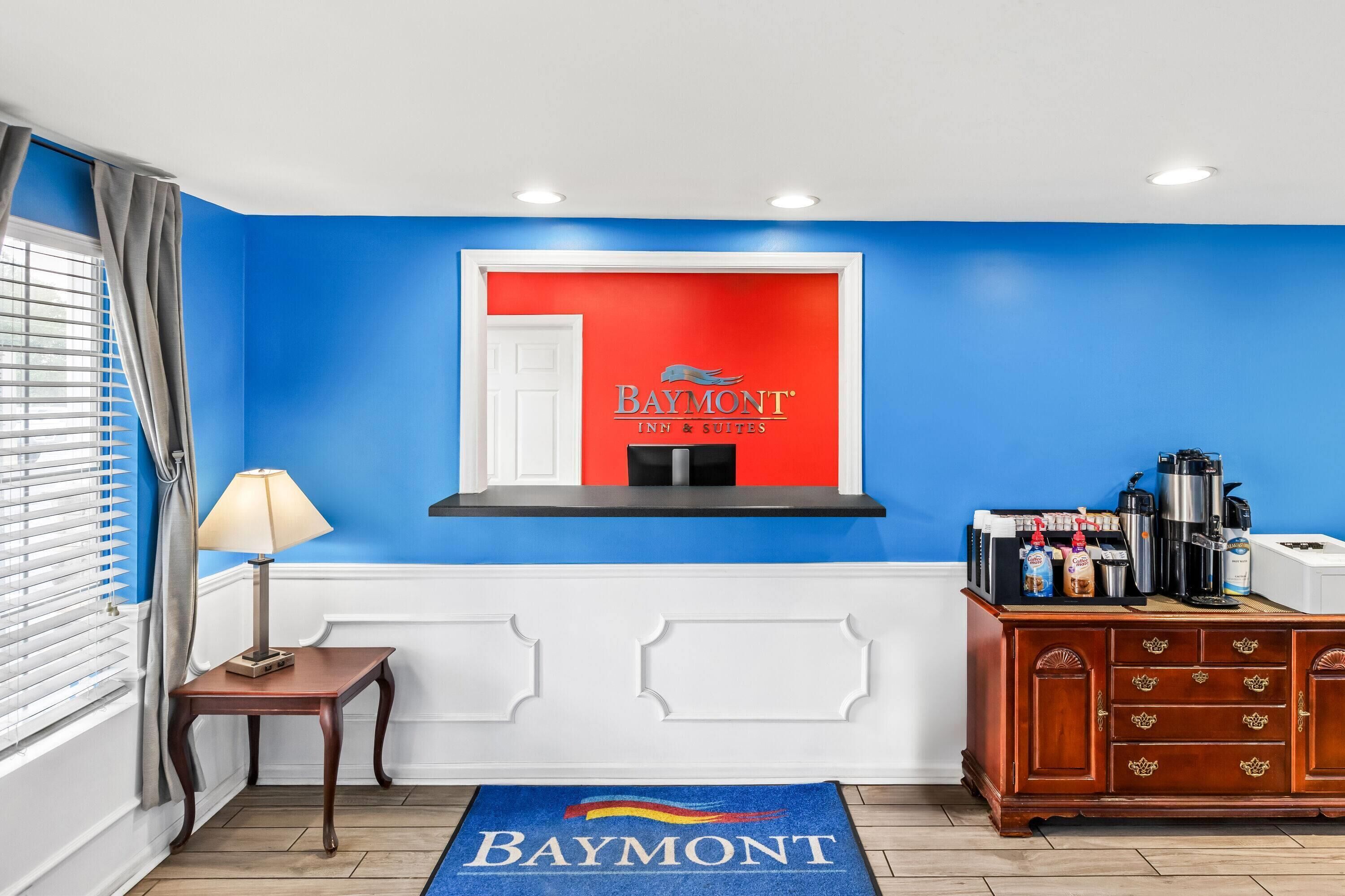 Un vestíbulo de hotel con pared azul, una recepción, una estación de café y un letrero de Baymont Inn & Suites.
