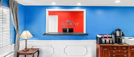 Un vestíbulo de hotel con pared azul, una recepción, una estación de café y un letrero de Baymont Inn & Suites.