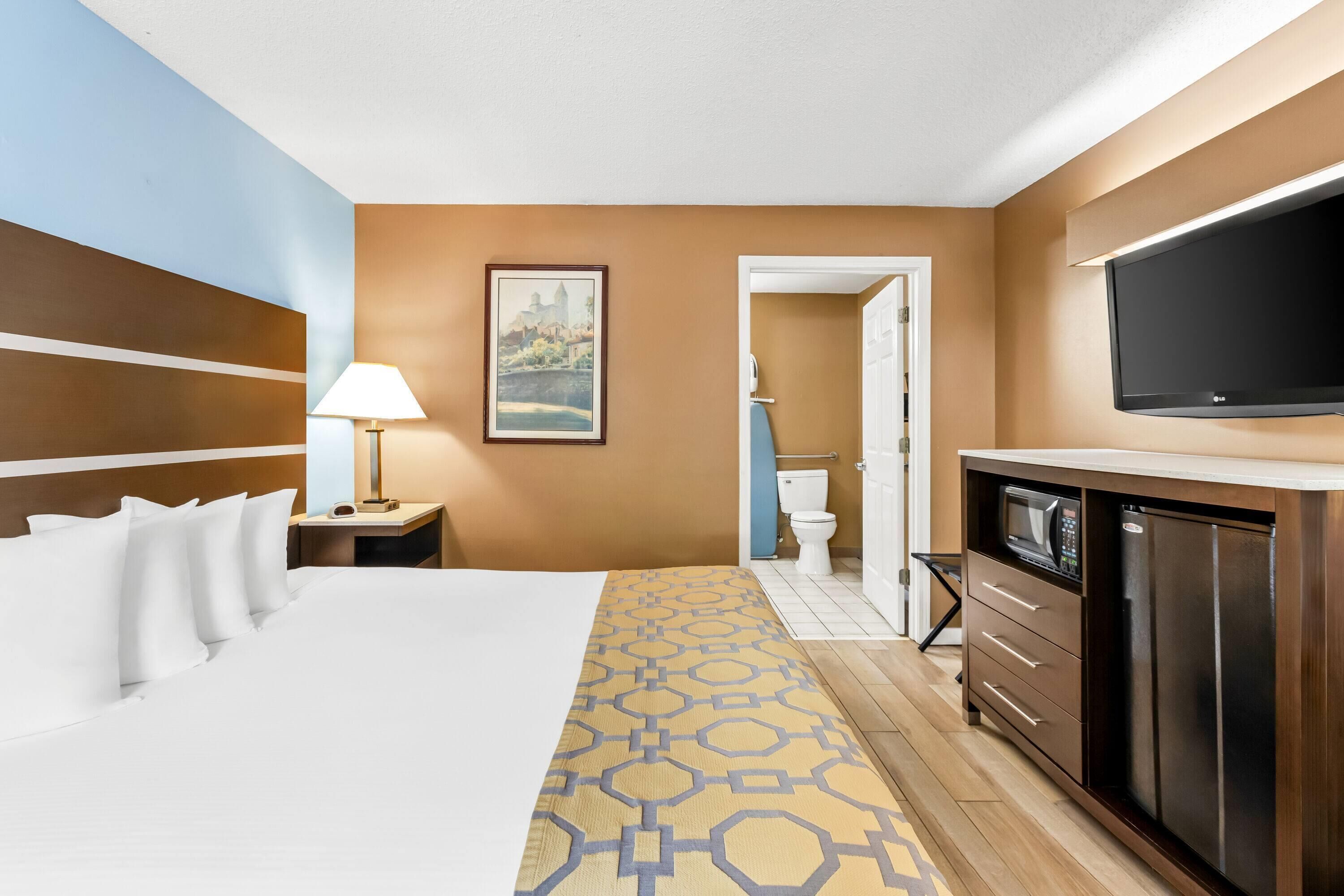 A hotel room with a bed, a desk with a lamp, a television, a microwave, and a refrigerator.