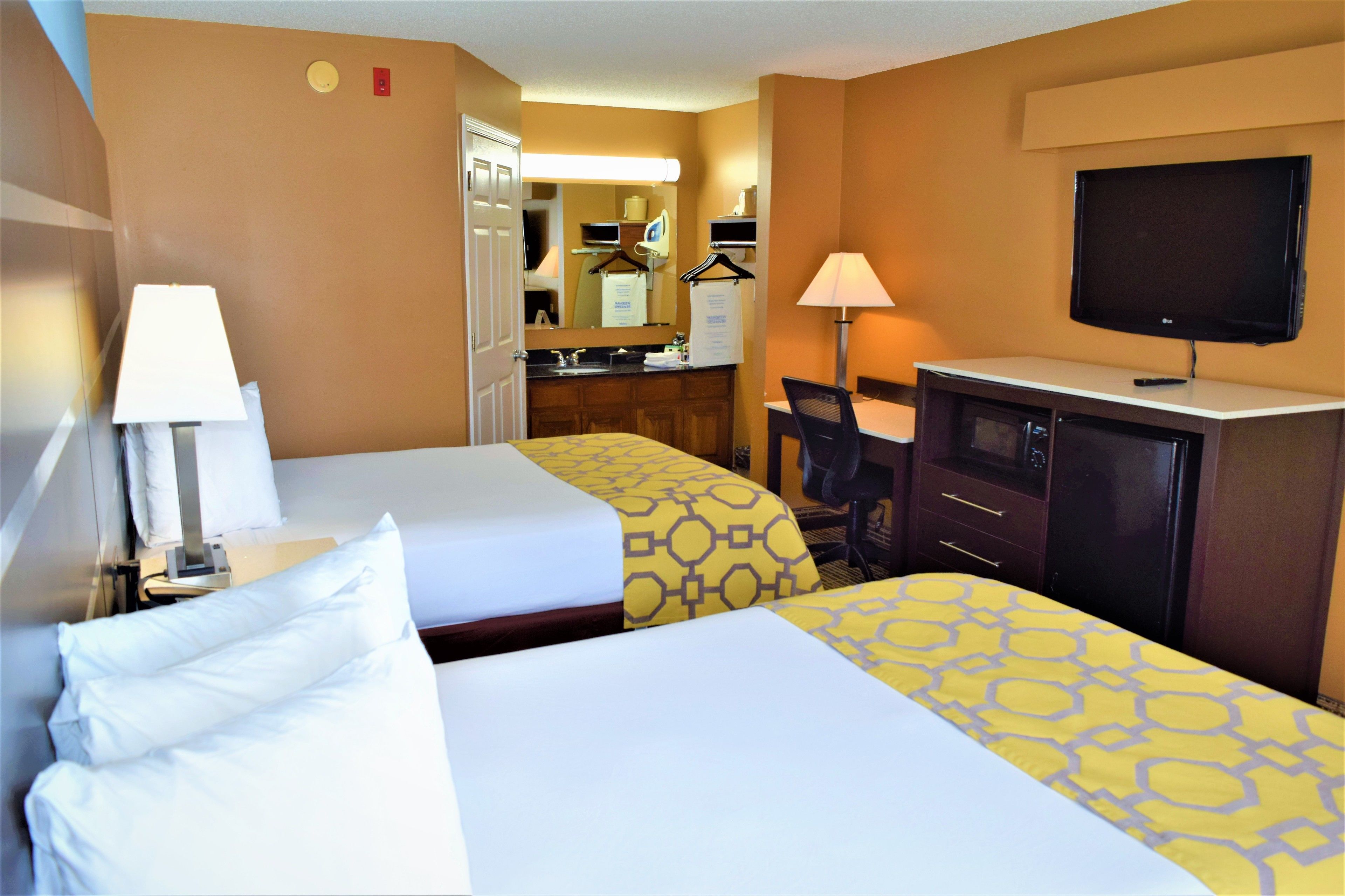 A hotel room with two beds, a desk, a chair, a TV, and a bathroom visible through an open door.