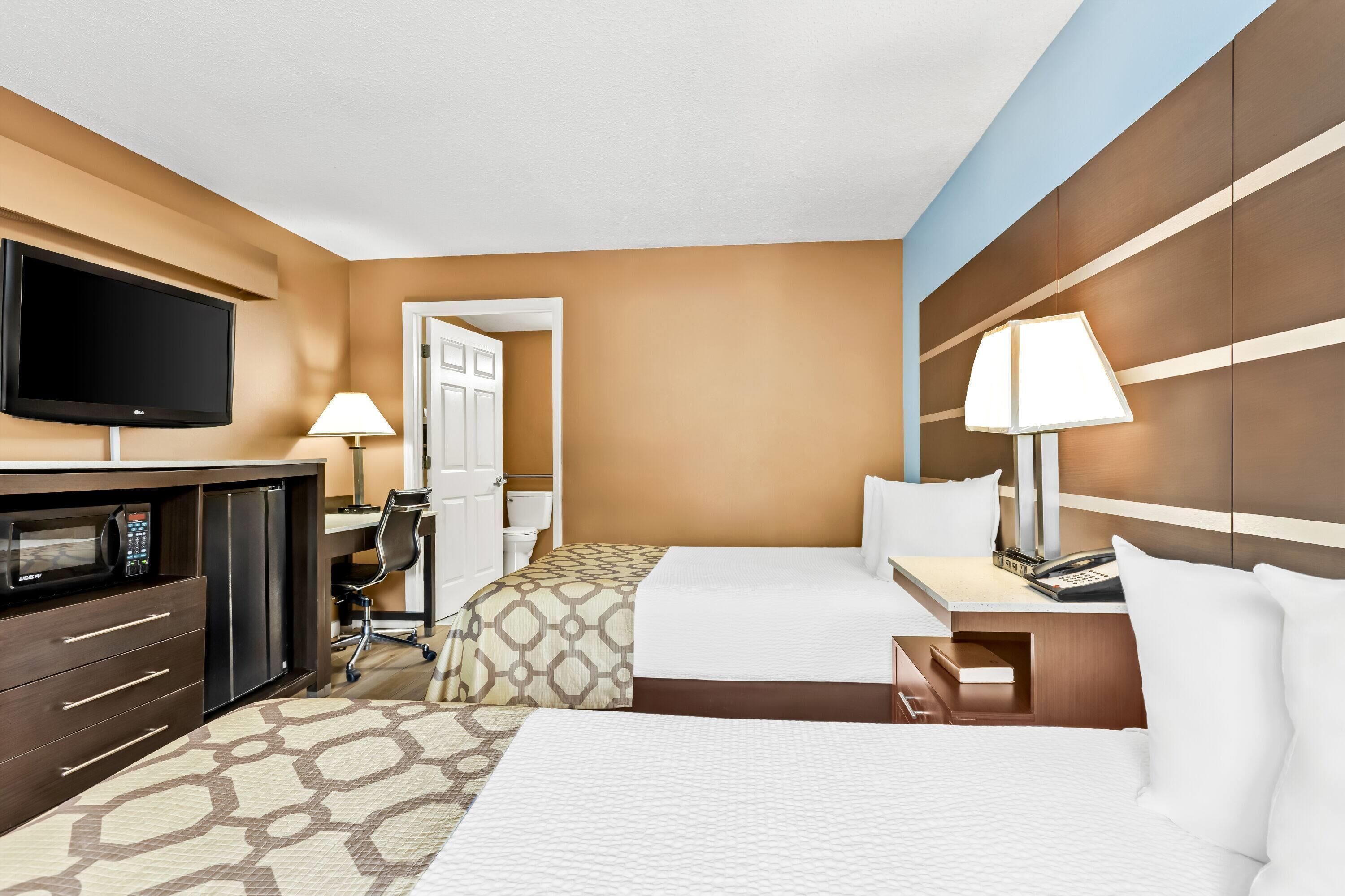 Une chambre d’hôtel avec deux lits, un bureau, une télévision, un four à micro-ondes et une porte de salle de bain.