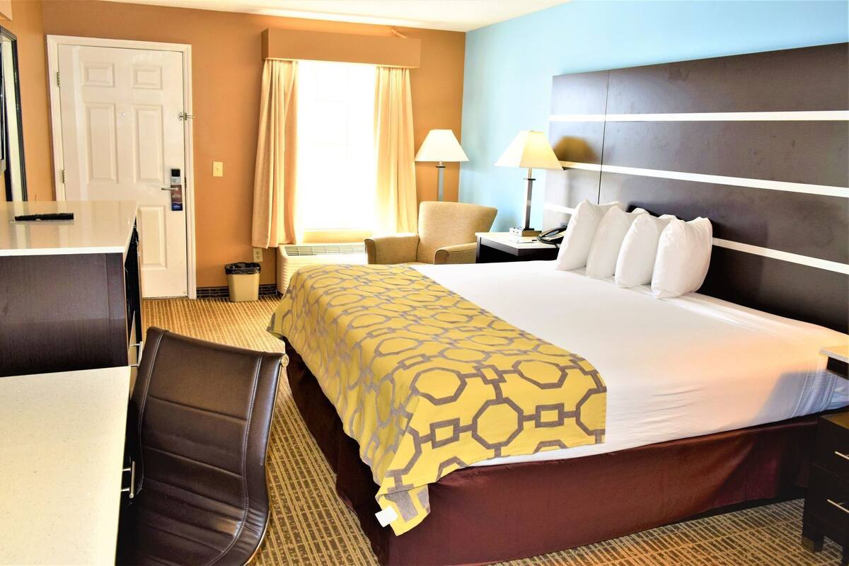 A hotel room with a bed, a desk, a chair, a lamp, and a TV.
