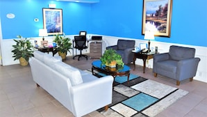 A living room with a blue wall, a white sofa, a grey armchair, a coffee table, and two side tables with lamps and decorative items. - Baymont by Wyndham Forest City (Forest City)