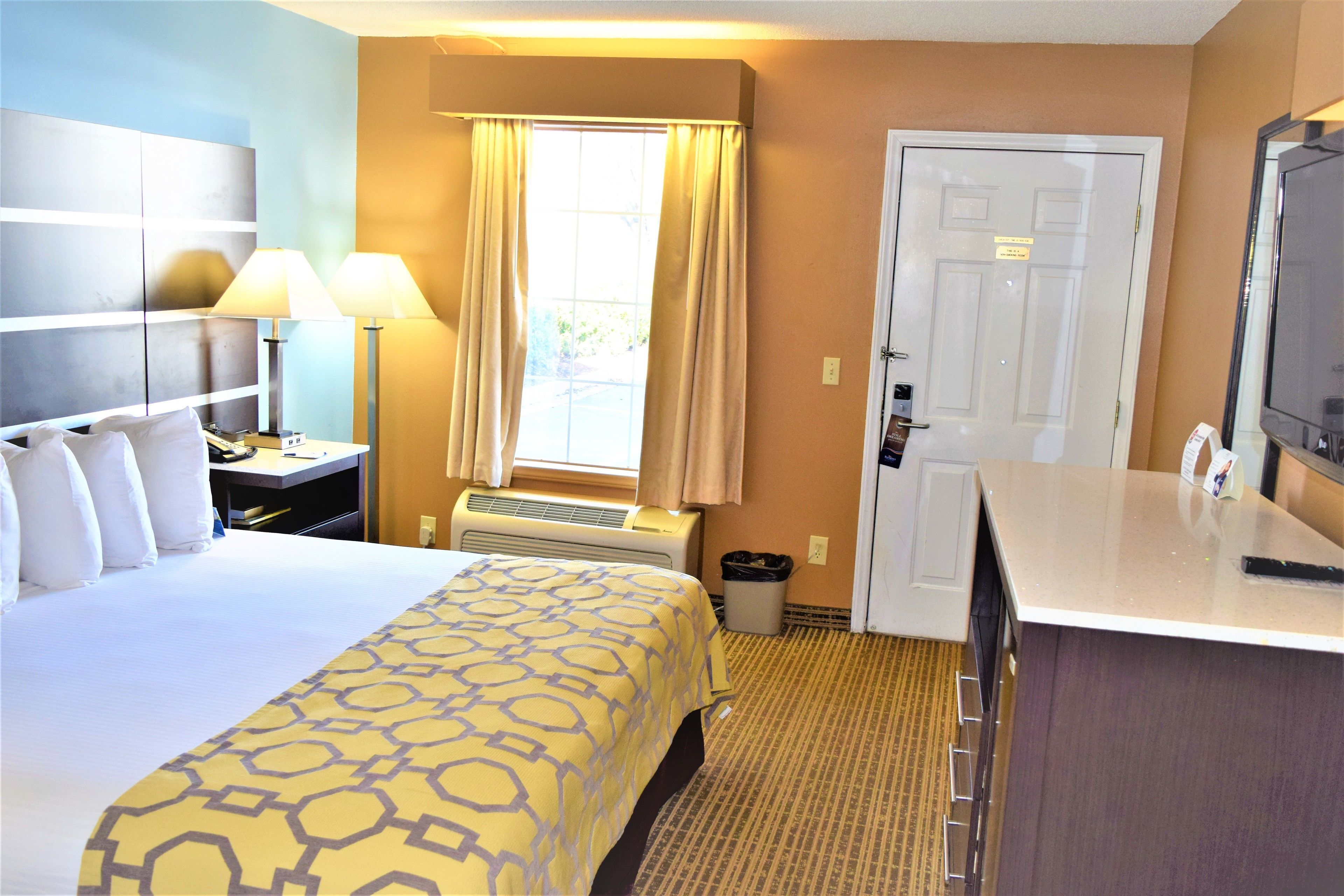 A hotel room with a bed, bedside lamps, a desk, a TV, and a window with curtains.