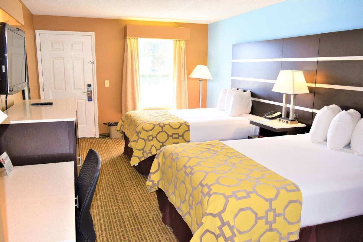 A hotel room with two beds, a desk, a chair, a TV, and a window with curtains.