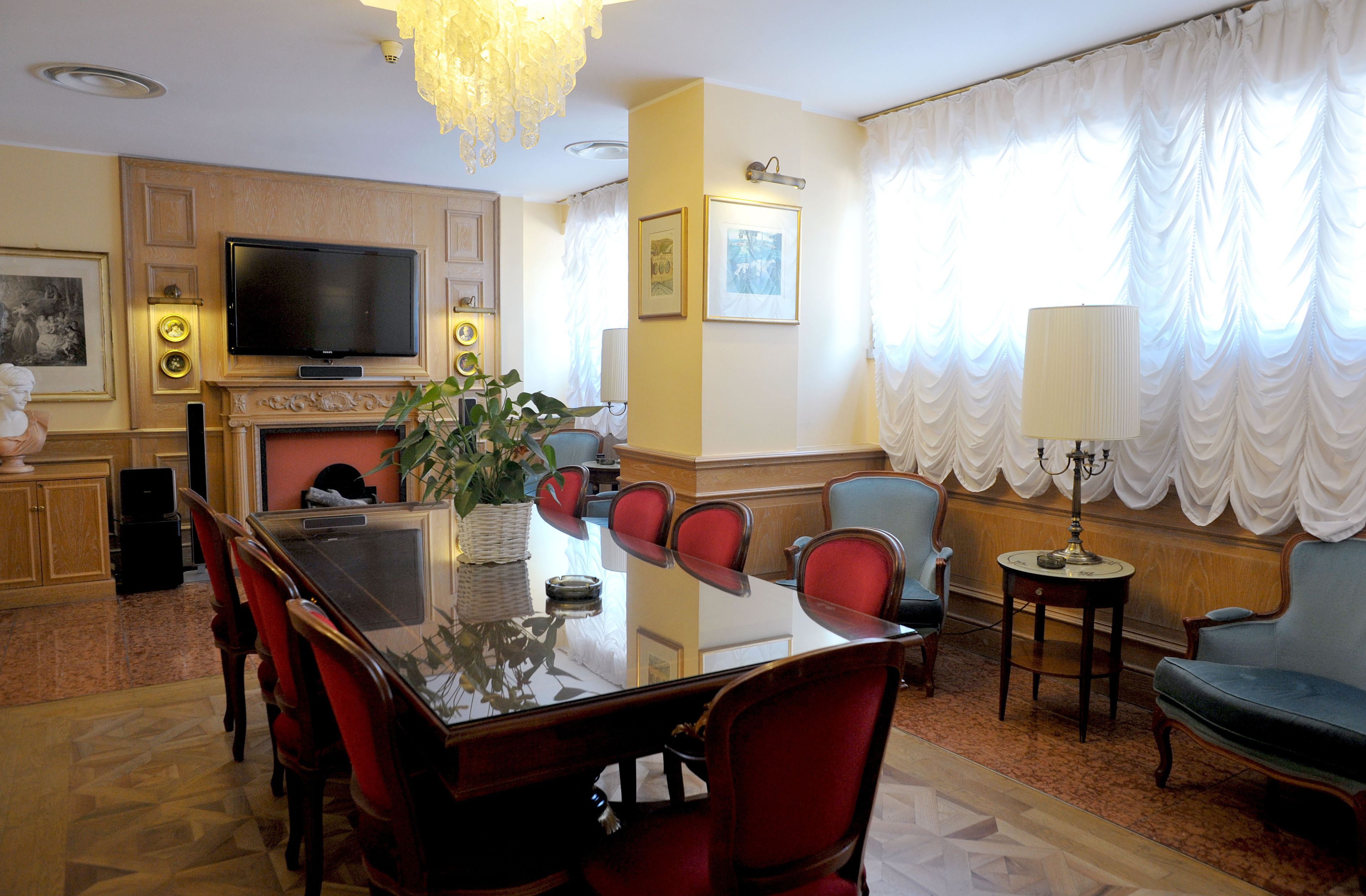 A hotel room with a dining table, chairs, a television, a fireplace, and a large window with curtains.
