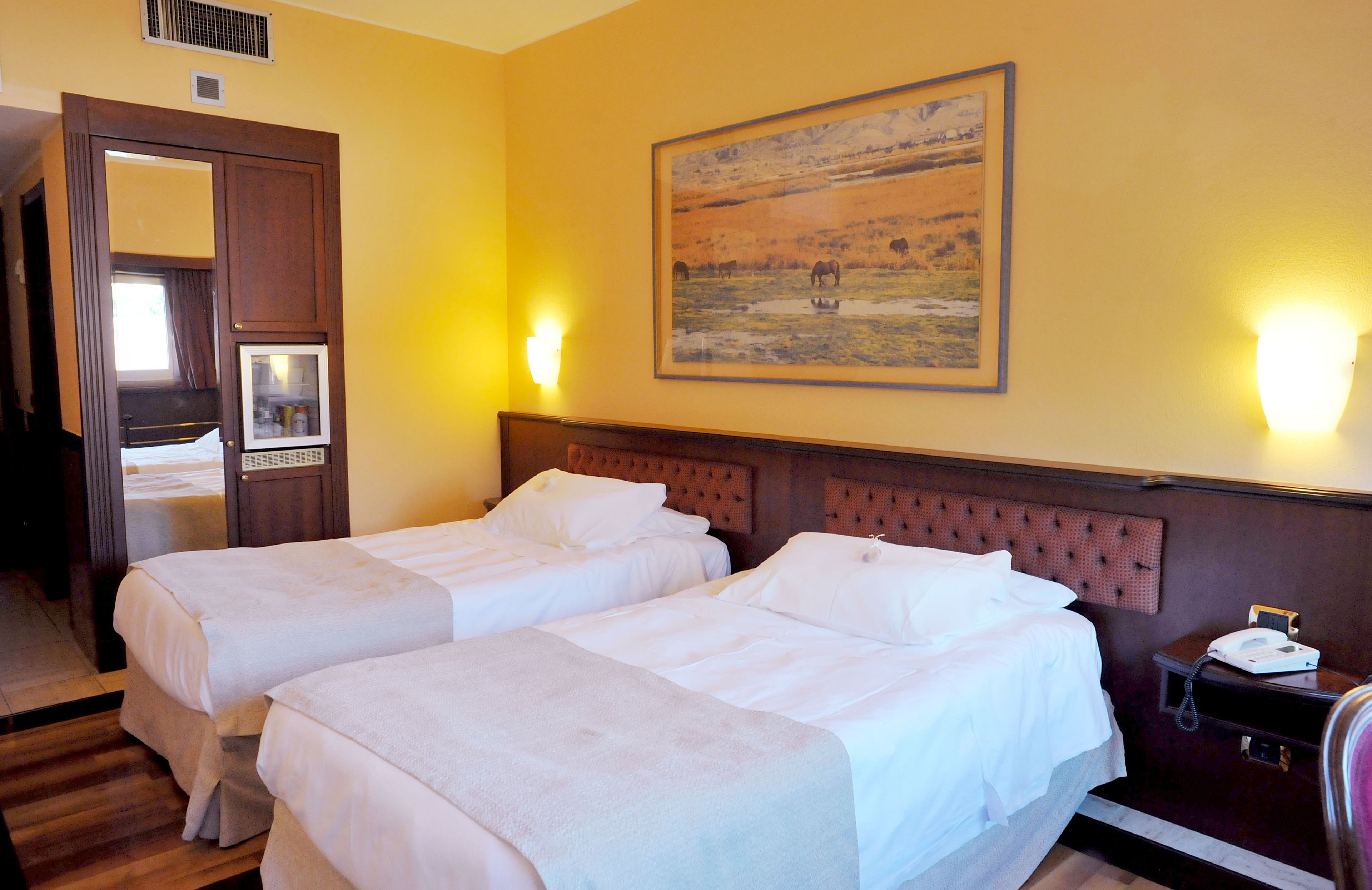 Quarto de hotel com duas camas, cabeceira de madeira, um quadro na parede e mesa de cabeceira com telefone.