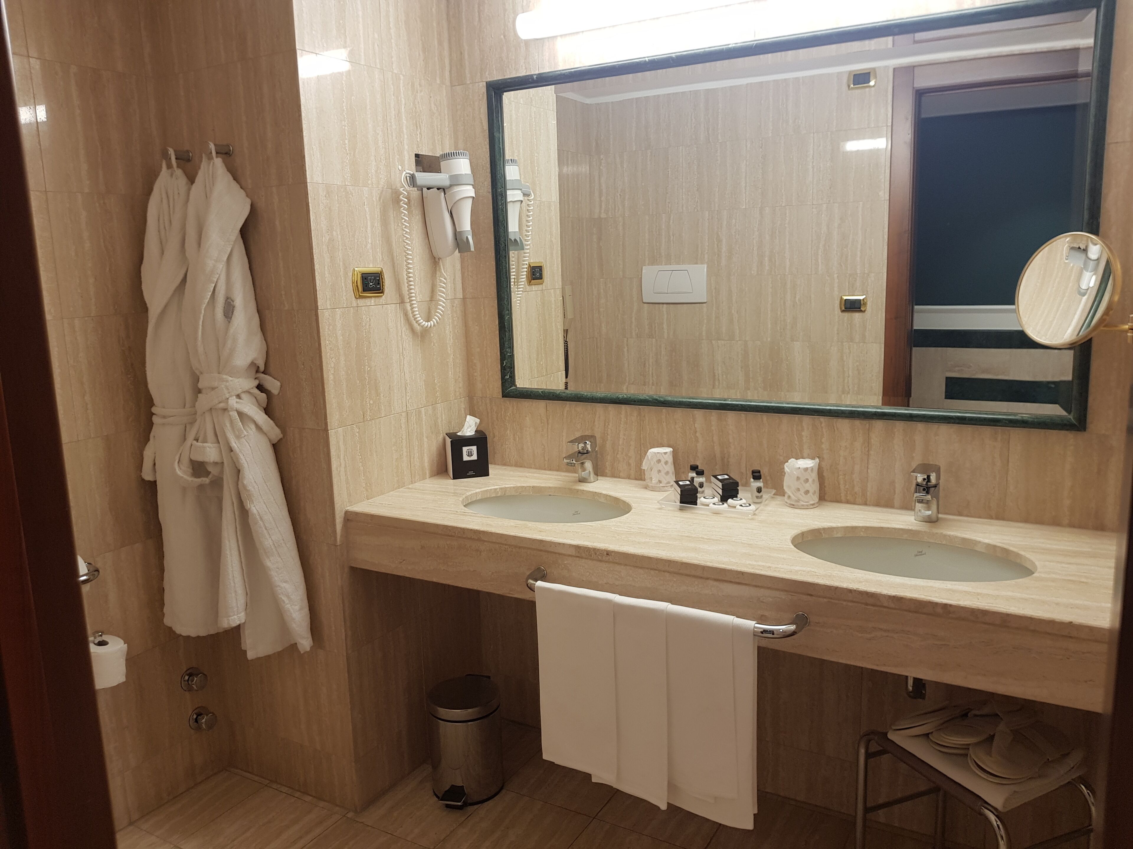 Ein Badezimmer mit zwei Waschbecken, einem großen Spiegel, einem an der Wand hängenden Bademantel und einem Fön.