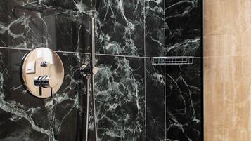 Un baño moderno con pared de ducha de mármol negro, zona de baño de madera y cerramiento de ducha de vidrio.