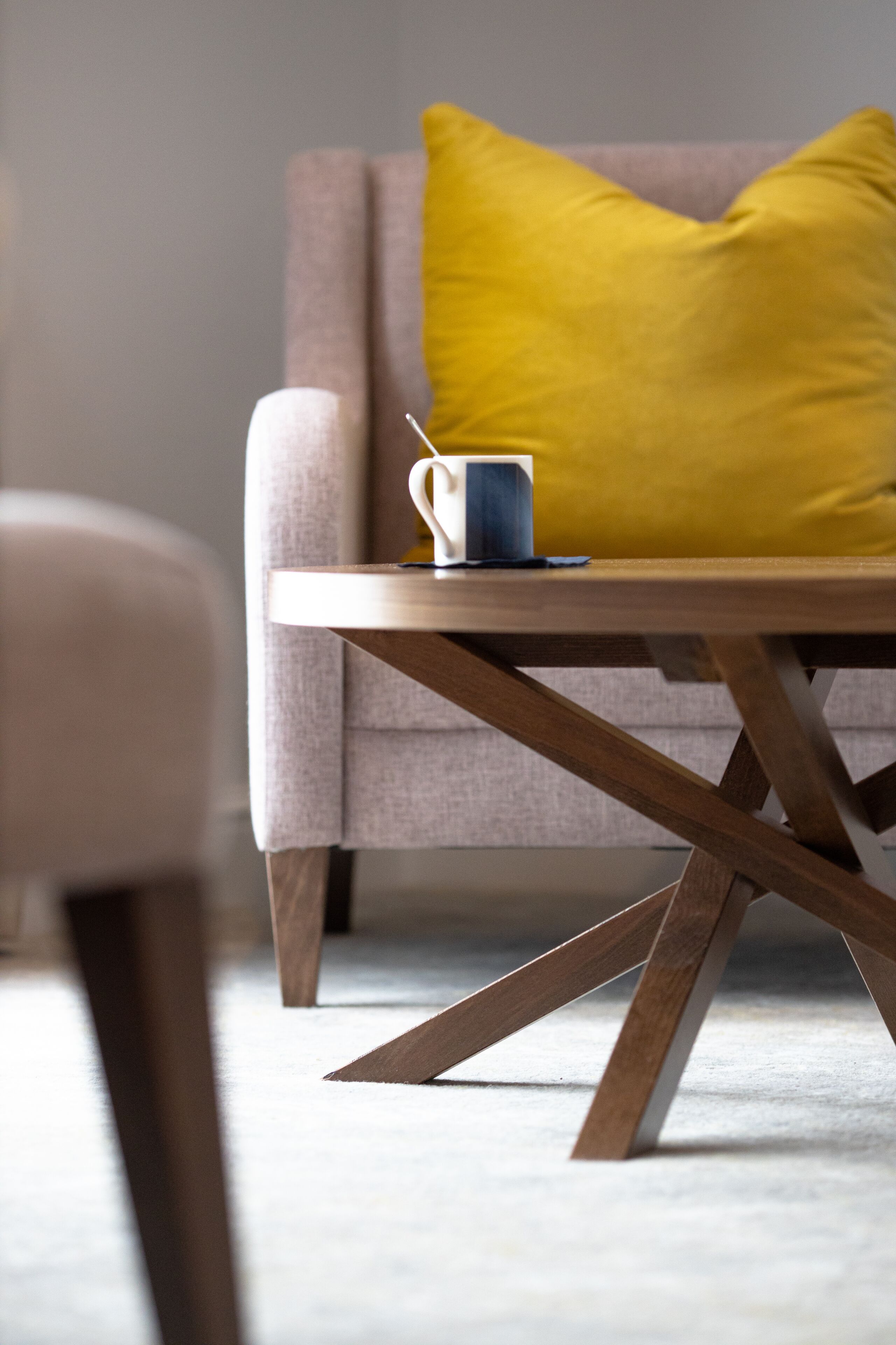A modern living room with a wooden coffee table, a sofa, and a bright yellow pillow.