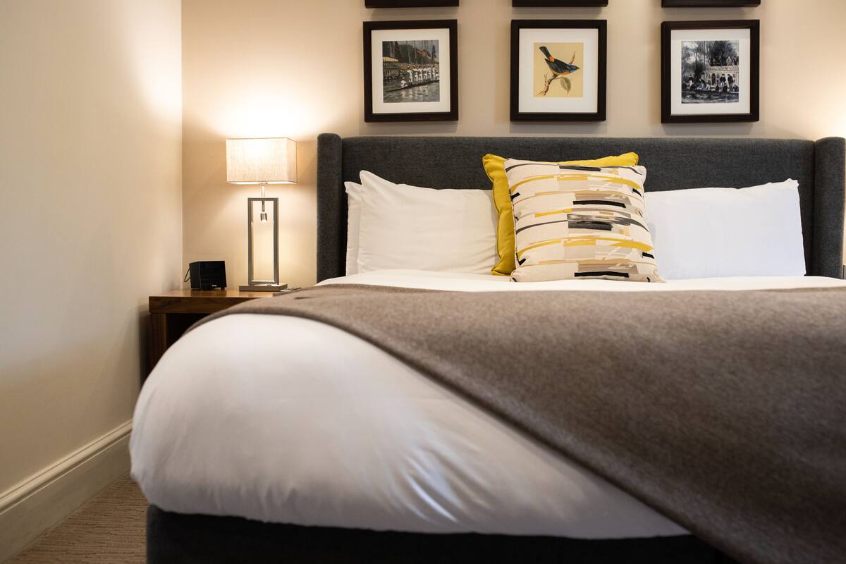 A neatly made bed with a grey headboard, white bedding, and a striped pillow. There are framed pictures on the wall above the bed.