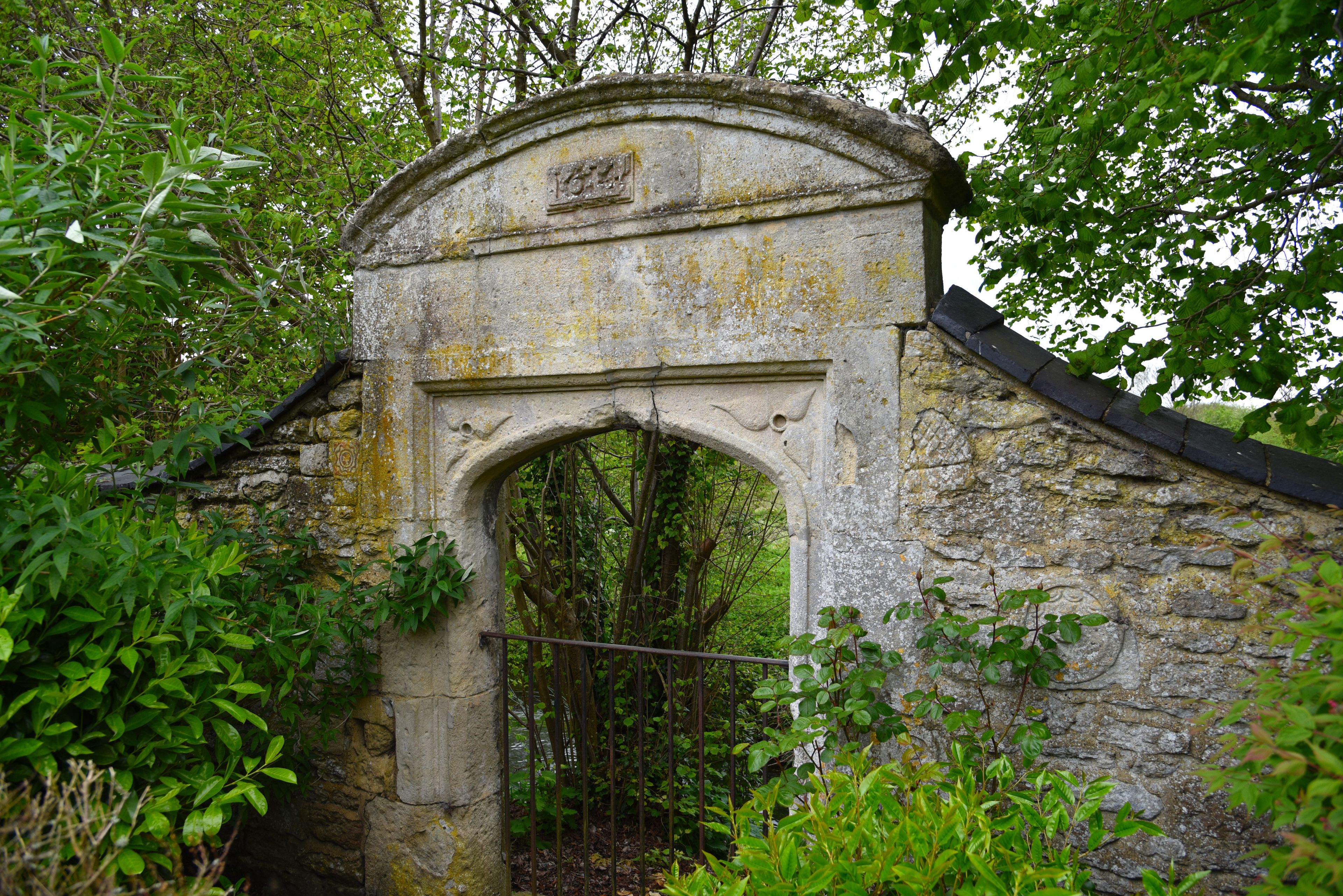 An old stone archway with a metal gate, surrounded by lush greenery.