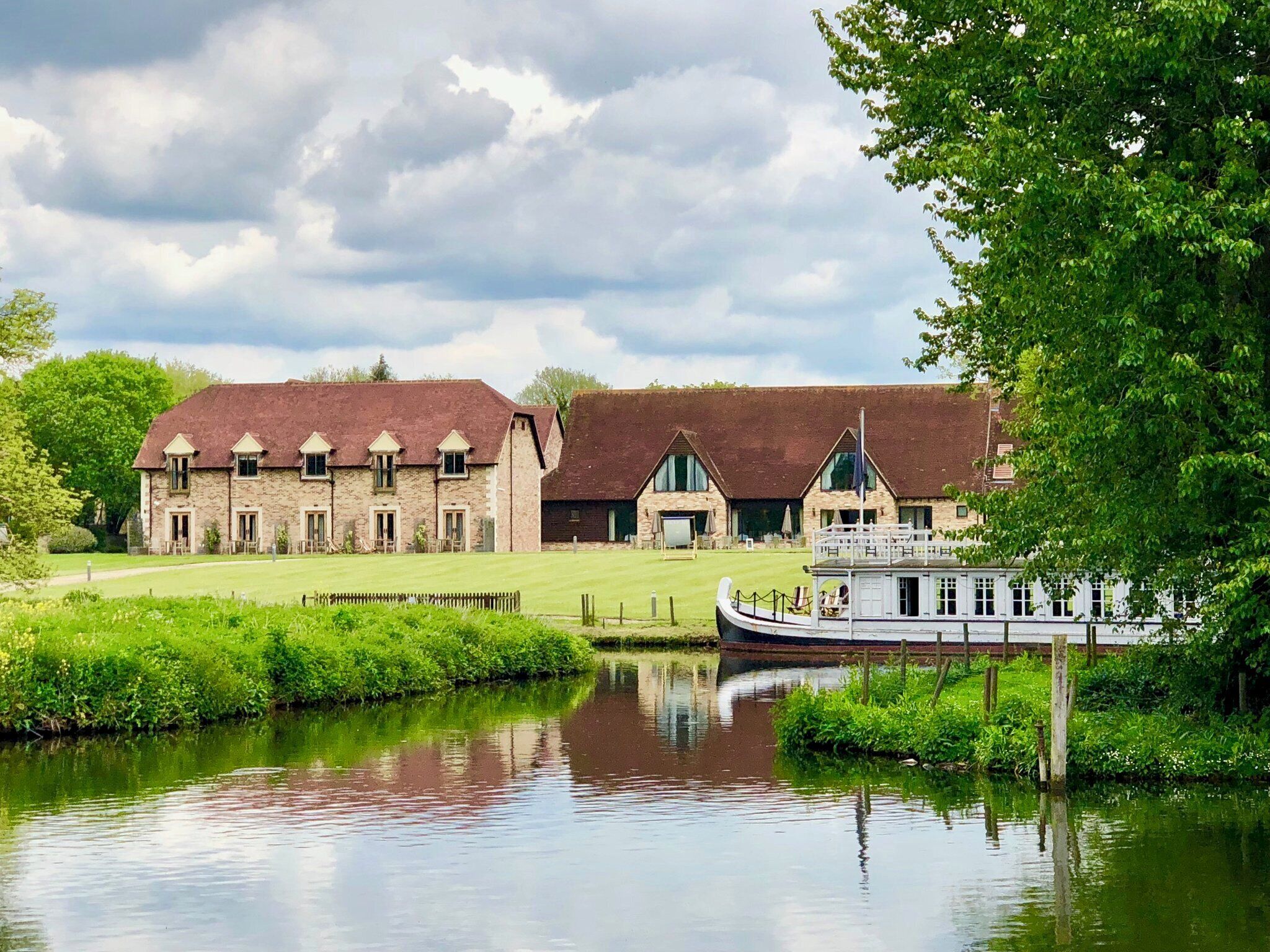 A riverside hotel with stone buildings, a boat dock, and a grassy lawn.