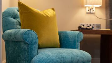 A teal armchair with a yellow pillow, a floor lamp, and a table with a lamp in a room with a carpeted floor.