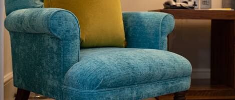 A teal armchair with a yellow pillow, a floor lamp, and a table with a lamp in a room with a carpeted floor.