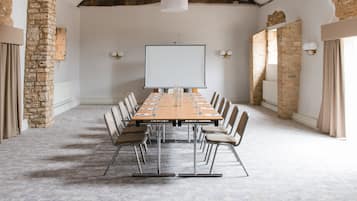 Un salón de conferencias con una larga mesa, sillas, una pantalla de proyector y paredes de piedra.