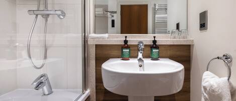 A modern bathroom with a glass-enclosed shower, a white sink with two soap dispensers, and a towel rack.