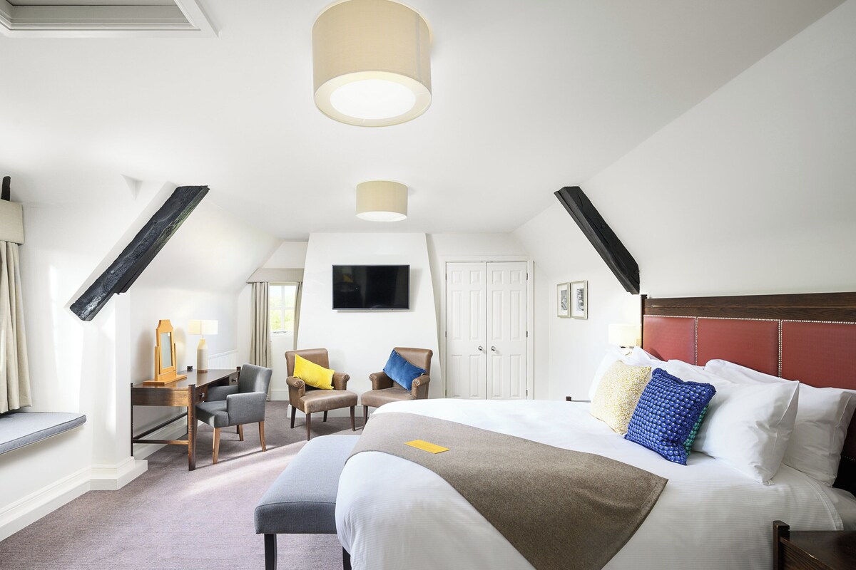 A hotel room with a bed, a desk, two chairs, a TV, and a window.