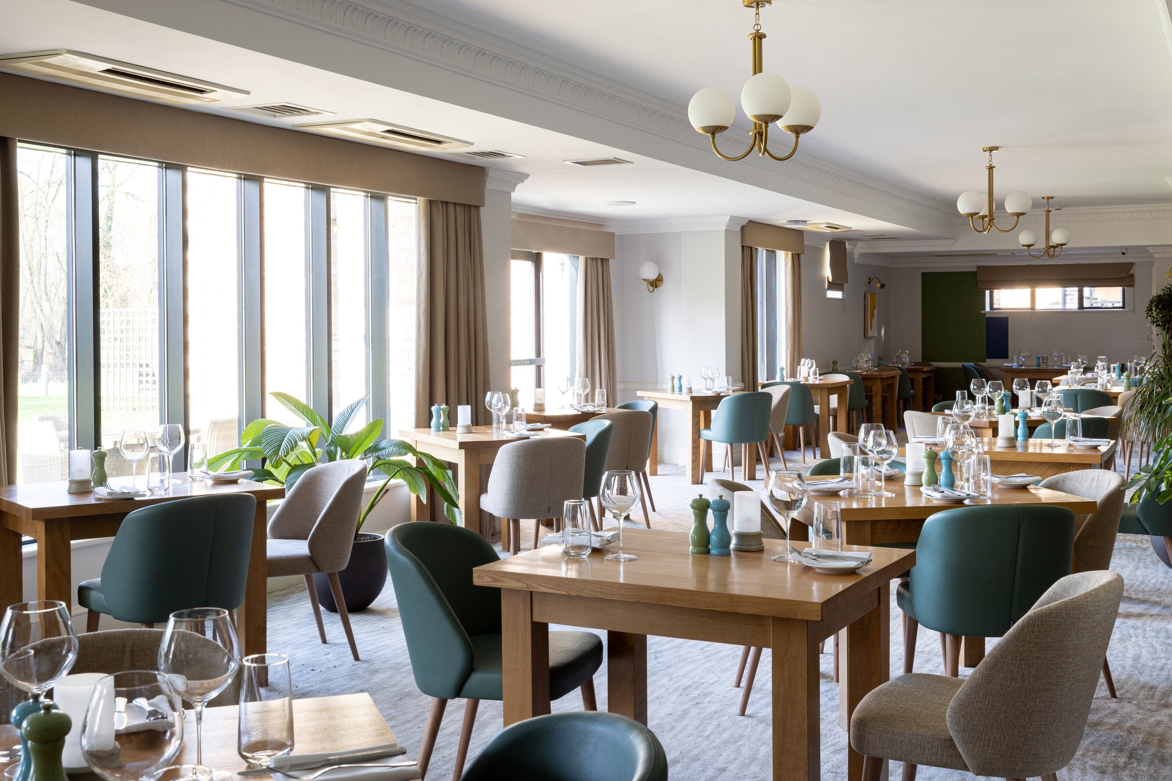 Un comedor bien iluminado con varias mesas y sillas, ventanas amplias y un candelabro.