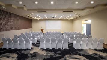 A conference room with rows of white chairs, a projector screen, and a carpeted floor.