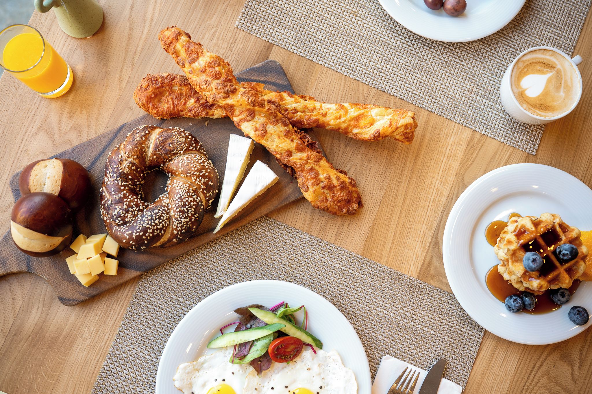 A breakfast table with various food items including waffles, eggs, and a bagel.