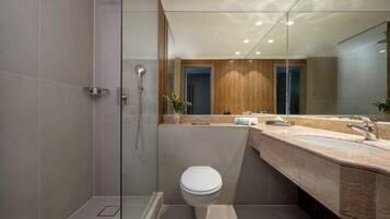 A modern bathroom with a glass-enclosed shower, a white toilet, and a vanity with a large mirror.