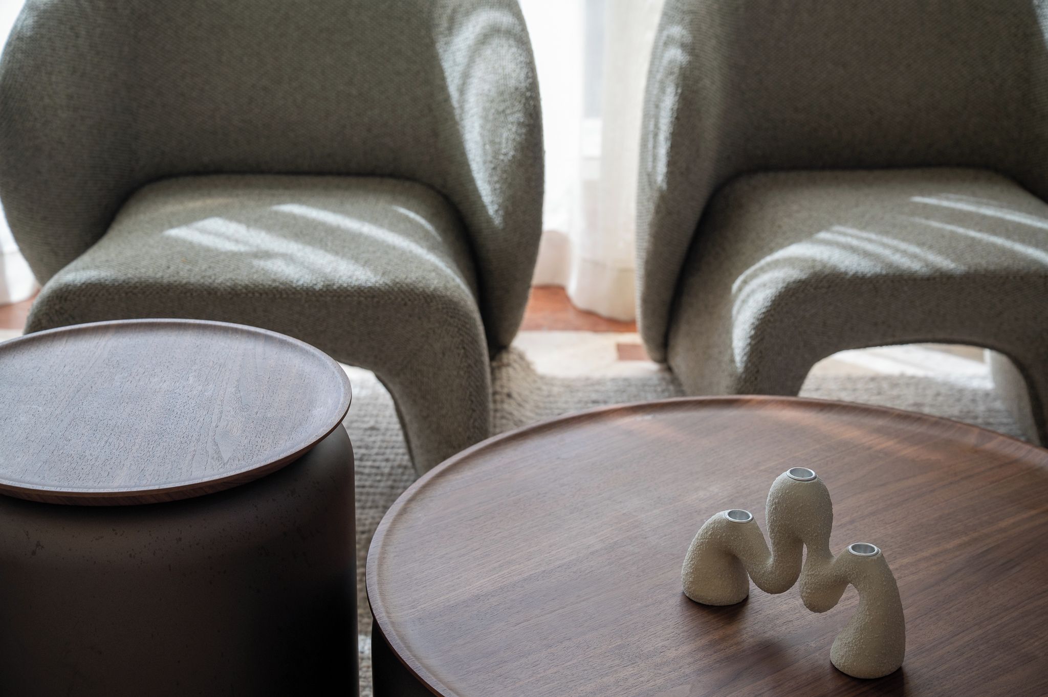 Un salon moderne avec deux fauteuils gris, une table basse ronde en bois et une petite table d’appoint ronde.