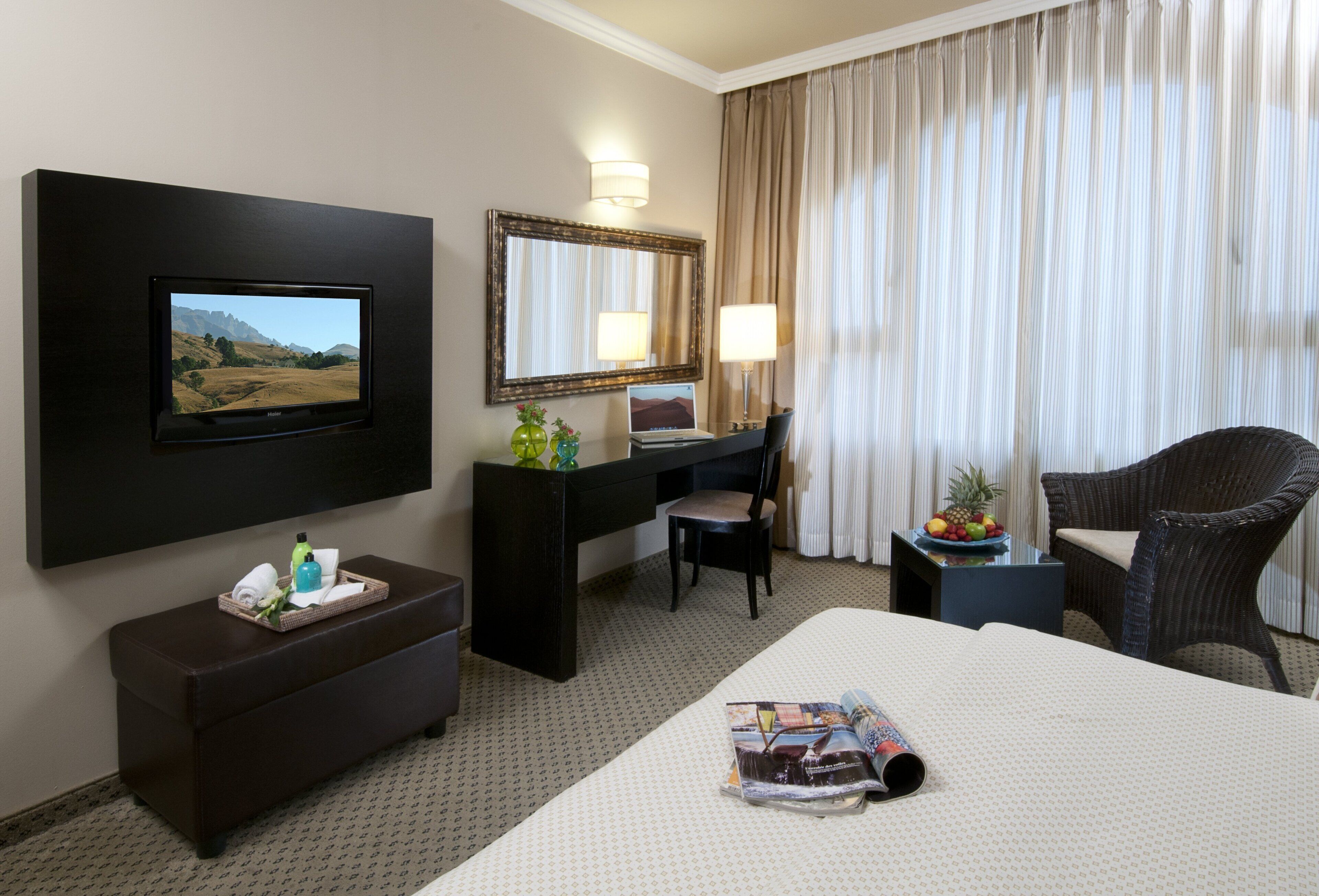 A hotel room with a bed, a desk, a chair, a TV, a mirror, and a window with curtains.