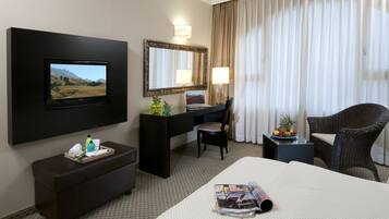 A hotel room with a bed, a desk, a chair, a TV, a mirror, and a window with curtains.