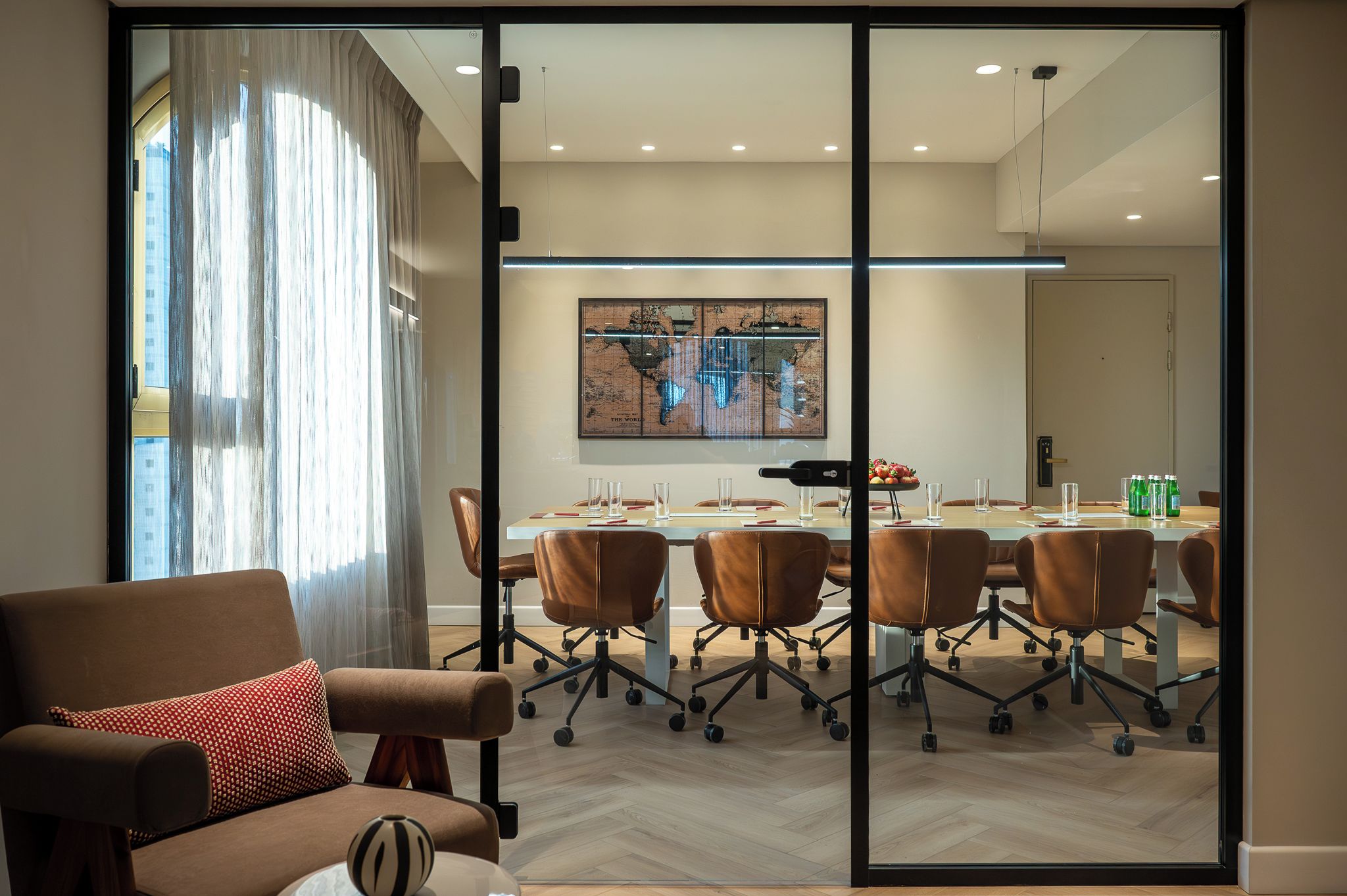 Een moderne vergaderruimte met een glazen scheidingswand, lederen stoelen, een houten tafel en een wereldkaart aan de muur.