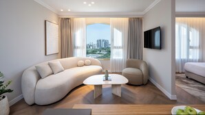 Un salón moderno con un sofá curvo, una mesa de centro y vistas de un paisaje urbano a través de amplios ventanales.