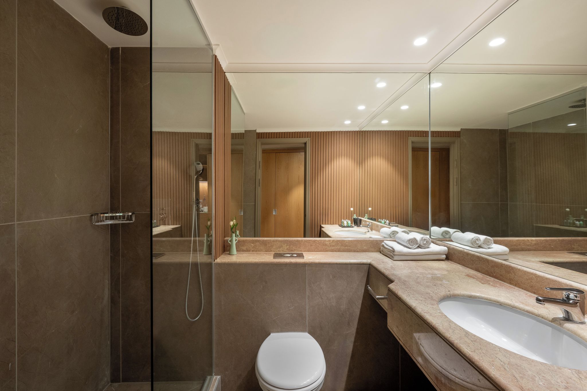Un baño moderno con cabina de ducha de vidrio, tocador con lavamanos y espejo, y un inodoro.