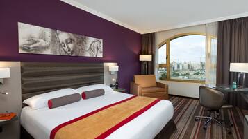 A hotel room with a large bed, a desk, a chair, and a view of the city.