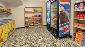 Zona de máquinas expendedoras con un refrigerador de Pepsi, estantes llenos de snacks y un suelo a cuadros.