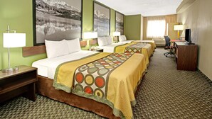 Habitación de hotel con tres camas, un escritorio con computadora y televisión.