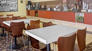 Un restaurante con varias mesas y sillas, una barra con diversos alimentos y bebidas, y una pizarra de menú.