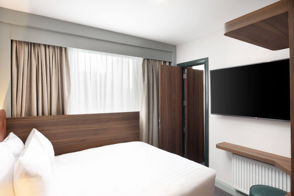 Una habitación de hotel con cama, cortinas, televisor y una estantería de madera.