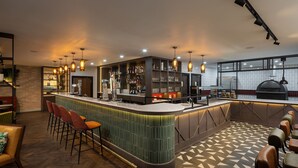 Zona de bar con mostrador curvo, taburetes y una sala de estar con piso estampado.