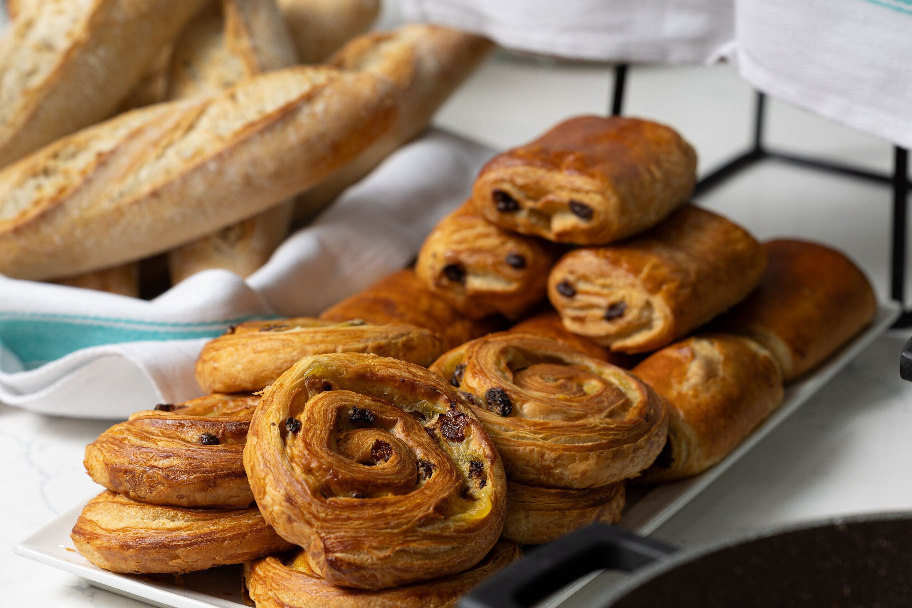 A tray of pastries, including croissants and bread rolls, arranged on a white plate.