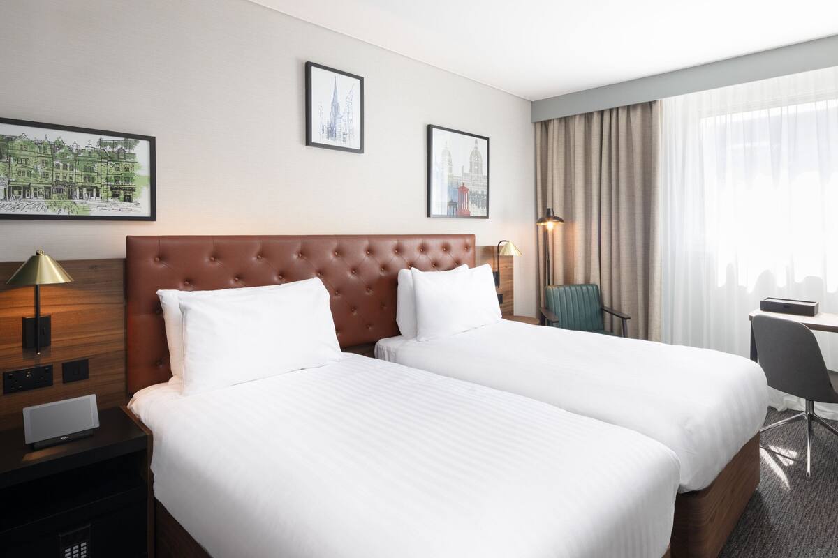 Habitación de hotel con dos camas, un escritorio, una silla y dos cuadros en la pared.