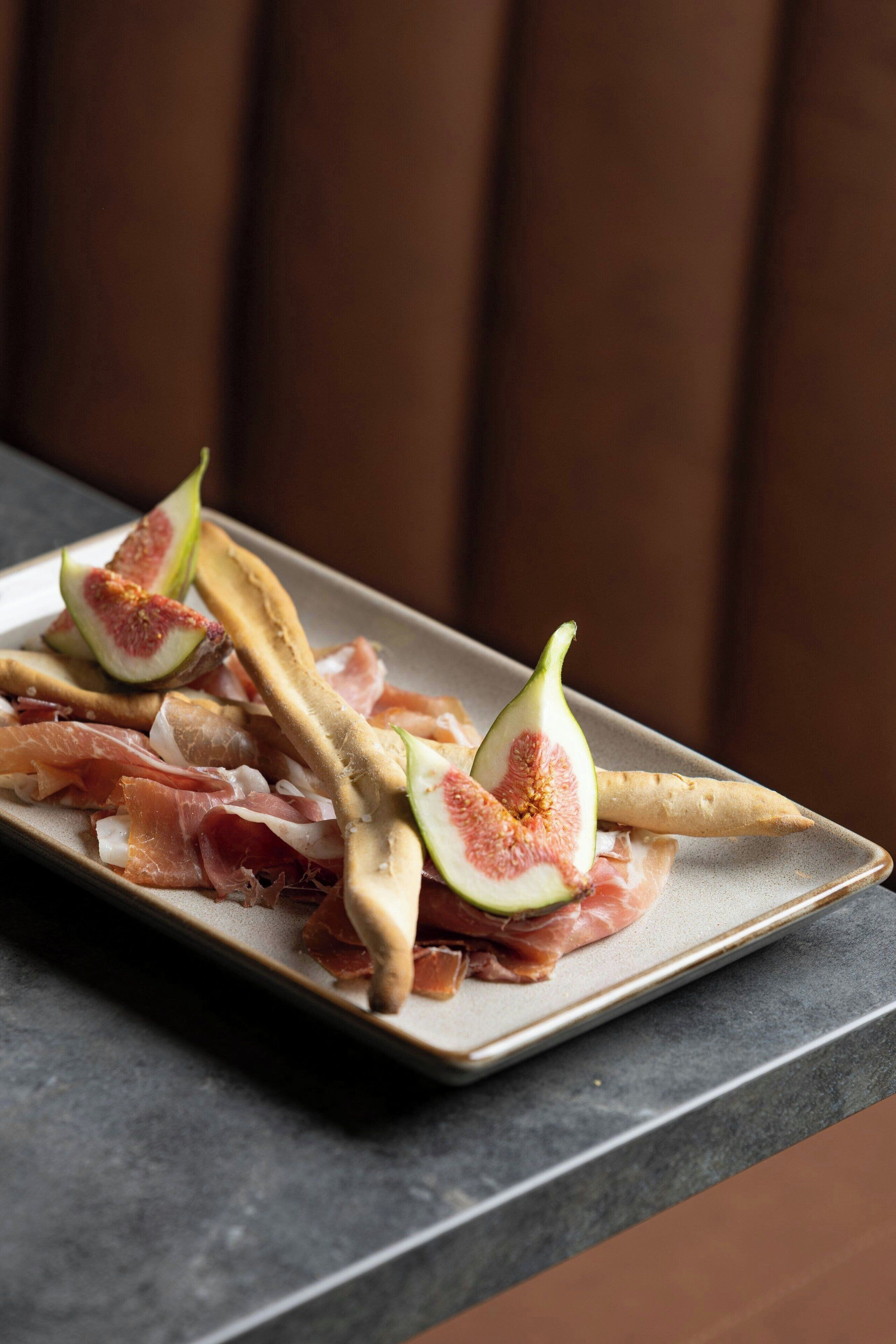 A plate of food with figs and prosciutto on a rectangular ceramic plate.