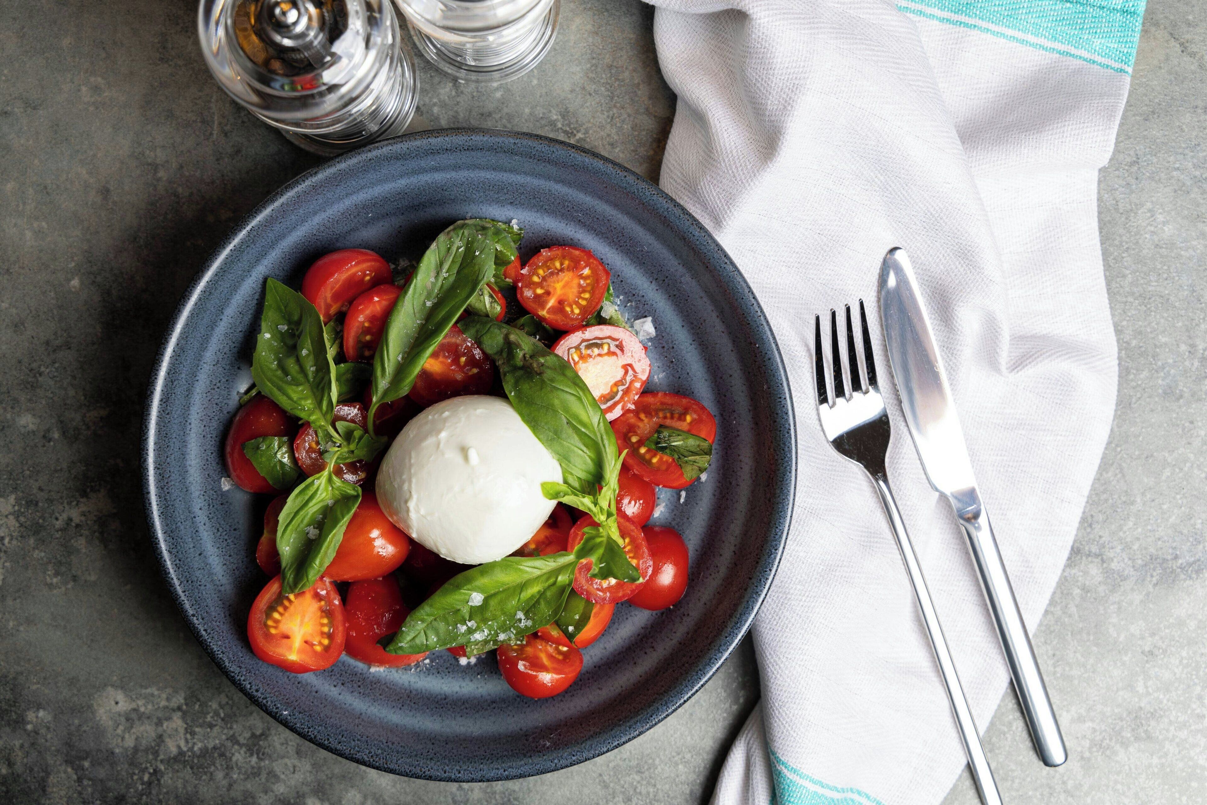 A plate with a white cheese, cherry tomatoes, and basil leaves.