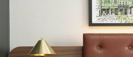 A hotel room with a wooden headboard, a bedside table with a lamp, a flat-screen TV, and a control panel.