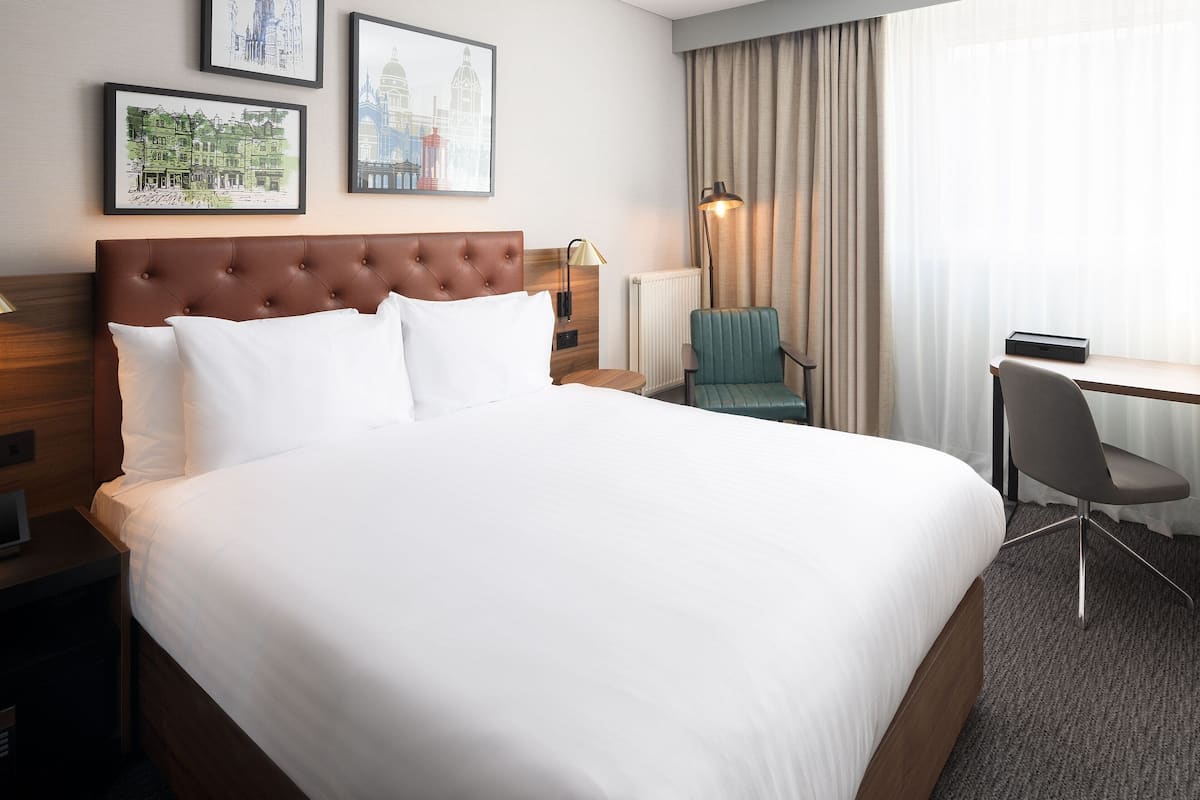 Habitación de hotel con una cama grande, un escritorio, una silla y dos cuadros en la pared.