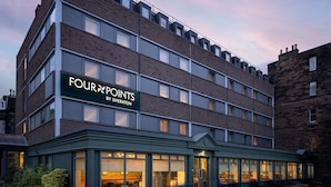 Un hotel de varios pisos con un letrero que dice "FOURPOINTS BY SHERATON" y una entrada a nivel de calle con puertas de vidrio.