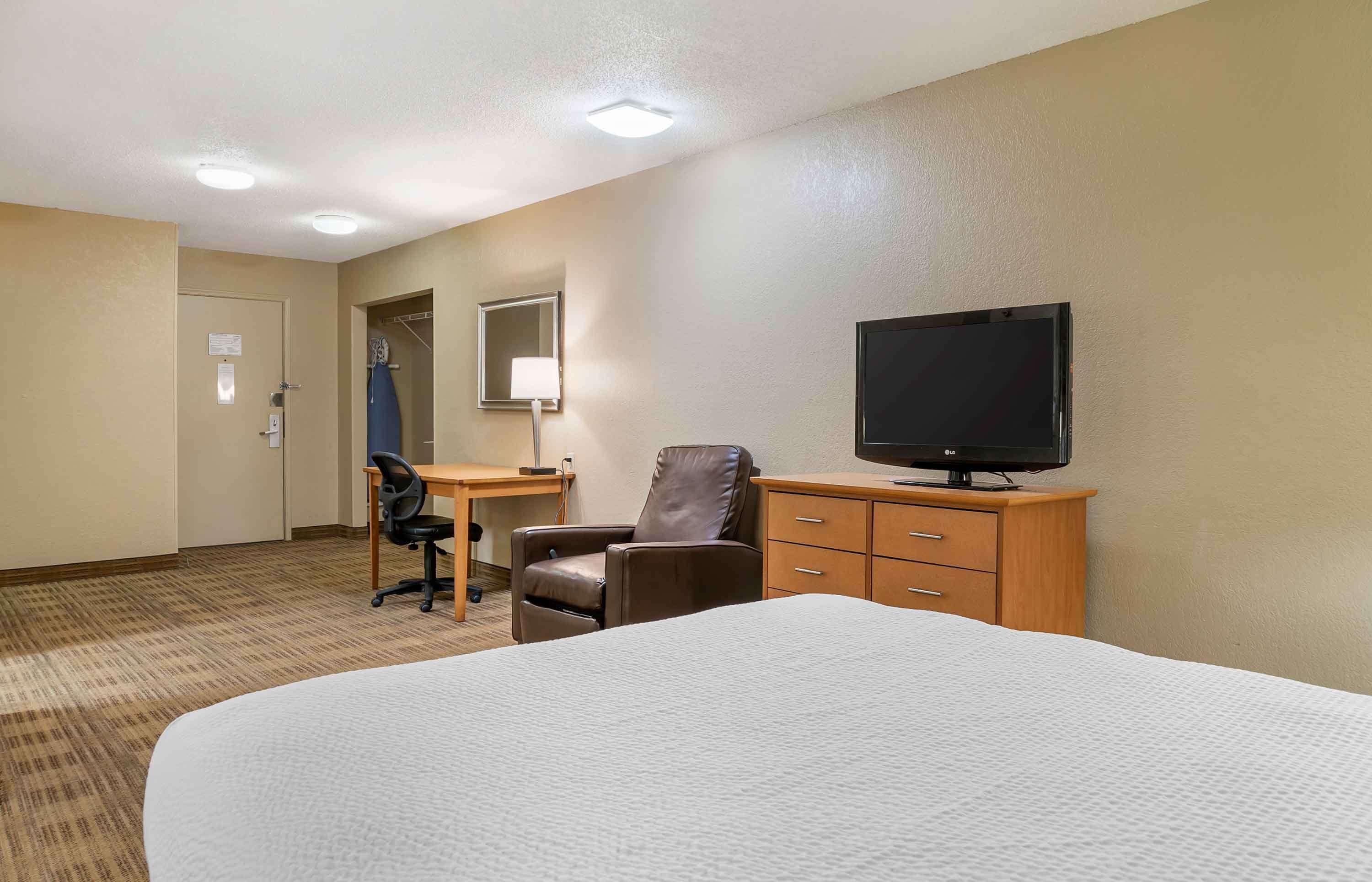 A hotel room with a bed, a desk with a chair, a television, and a wardrobe.