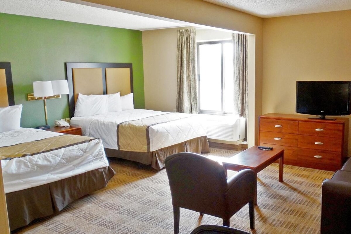 A hotel room with two beds, a television, a desk, and a chair.