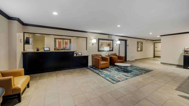 A reception area with a black reception desk, leather chairs, a blue rug, and a 'WELCOME' sign. - Extended Stay America Suites Oklahoma City Northwest (Oklahoma City)