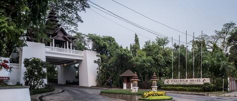 The entrance of Chatrium Hotel with a traditional architectural style, a landscaped garden, and a clear sky.